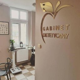 Copypoint - Wnętrze gabinetu dietetycznego z logo w kształcie jabłka i napisem 'Gabinet Dietetyczny' na ścianie, w tle waga diagnostyczna i okno.