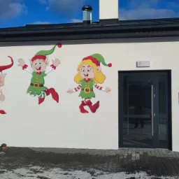 Kolorowe postacie elfów w świątecznych strojach namalowane na białej ścianie budynku, widoczne drzwi wejściowe i okno.