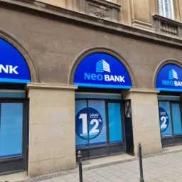 Elewacja budynku banku z trzema szyldami Neo Bank z logo i napisem, na oknach naklejki z ofertą lokat.