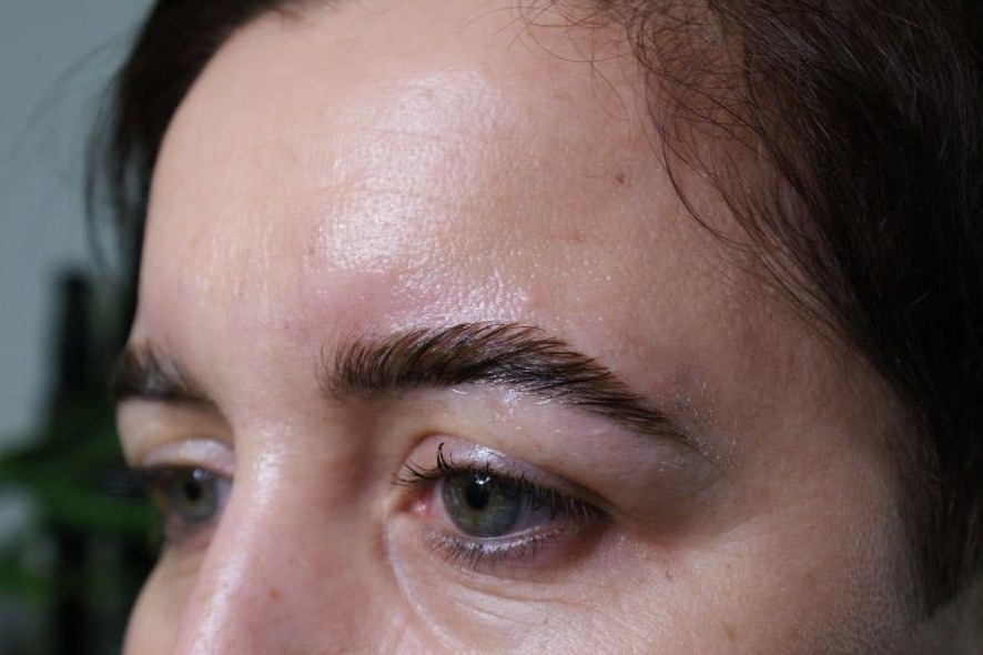 Zbliżenie na brwi po zabiegu laminacji, widoczne błyszczące włoski i nawilżona skóra wokół łuku brwiowego, delikatny makijaż oka.