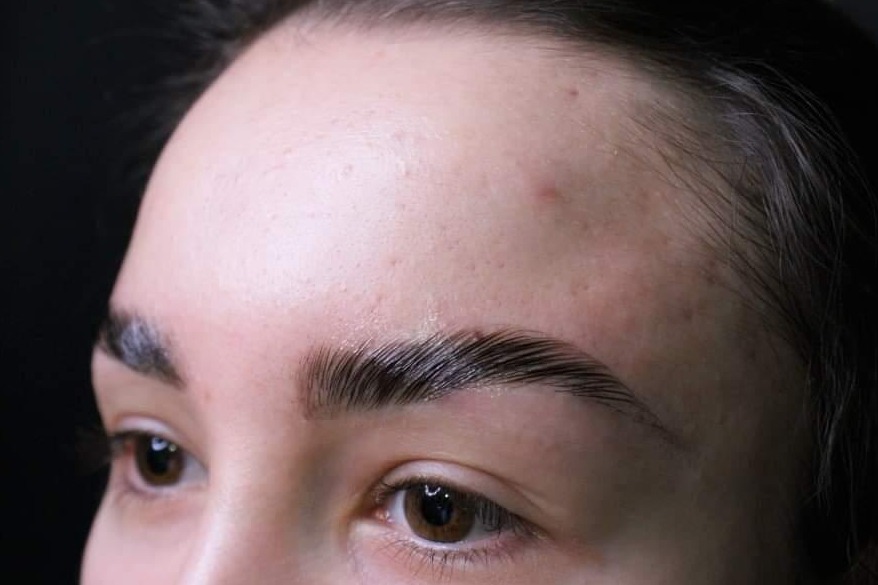 Zbliżenie na brwi po zabiegu laminacji, widoczne błyszczące, idealnie ułożone włoski i naturalny kształt łuku brwiowego.