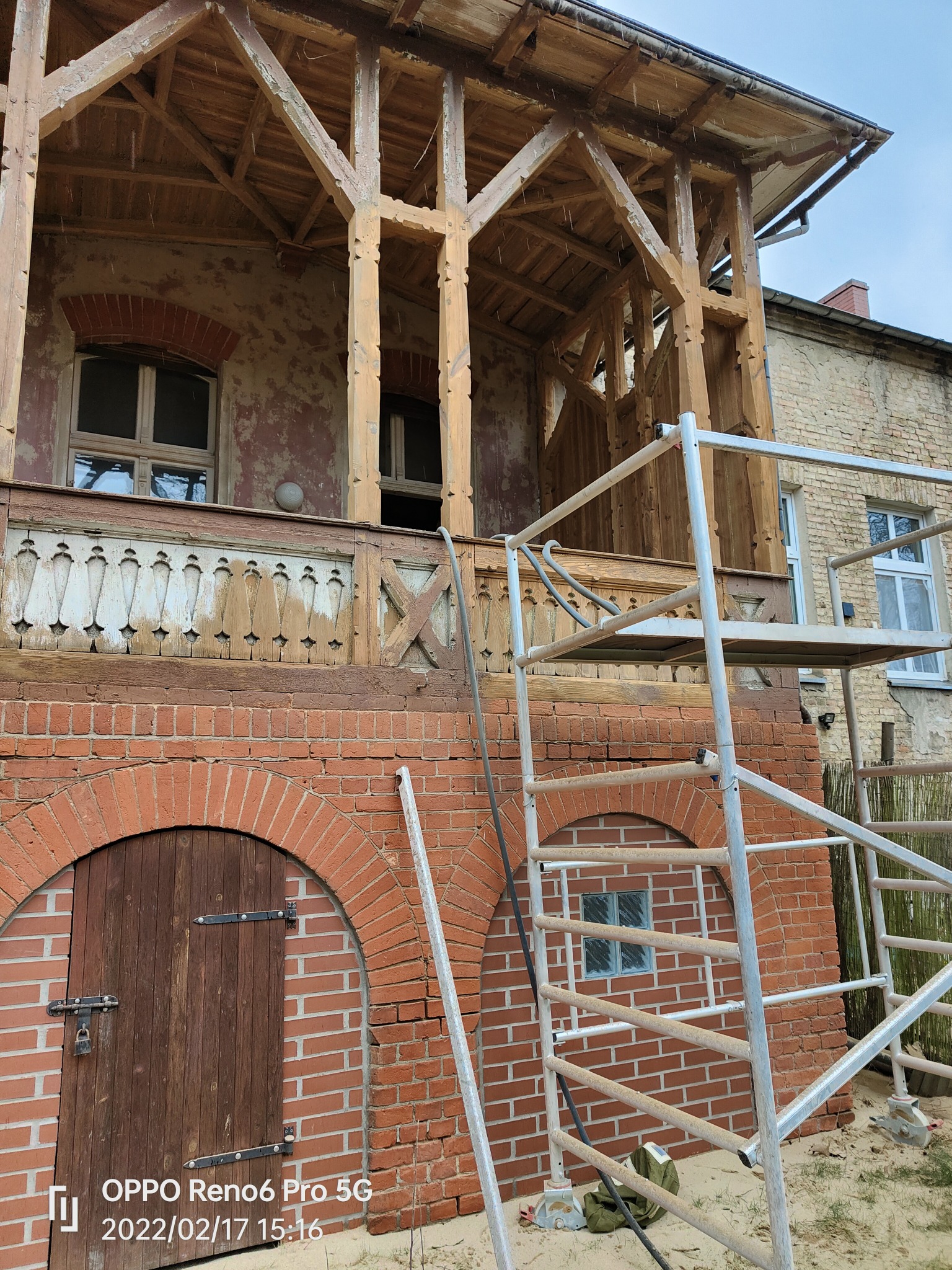 Drewniana konstrukcja balkonu starego budynku w trakcie renowacji, widoczne ślady starej farby i rusztowanie.
