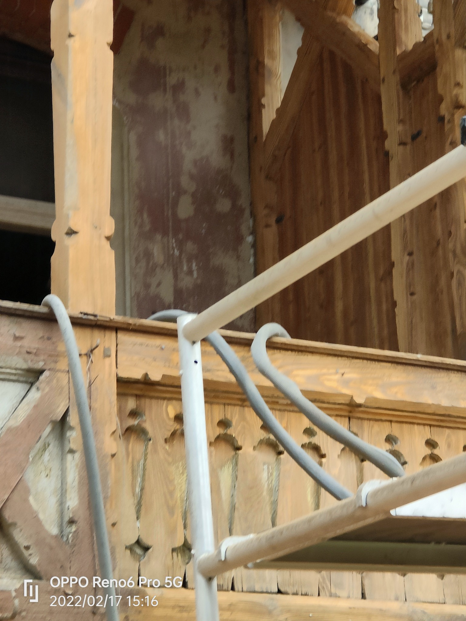 Drewniana konstrukcja balkonu w trakcie renowacji, widoczne ślady starej farby i rusztowanie.