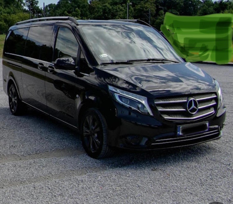 Czarny, luksusowy van Mercedes-Benz V-klasa z relingami dachowymi, zaparkowany na żwirowym parkingu w słoneczny dzień.