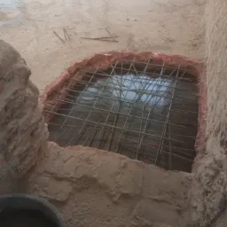 Zbrojenie w wykopie fundamentowym, widoczne pręty zbrojeniowe tworzące siatkę, przygotowane do zalania betonem, obok fragment starego muru i wiadro z zaprawą.