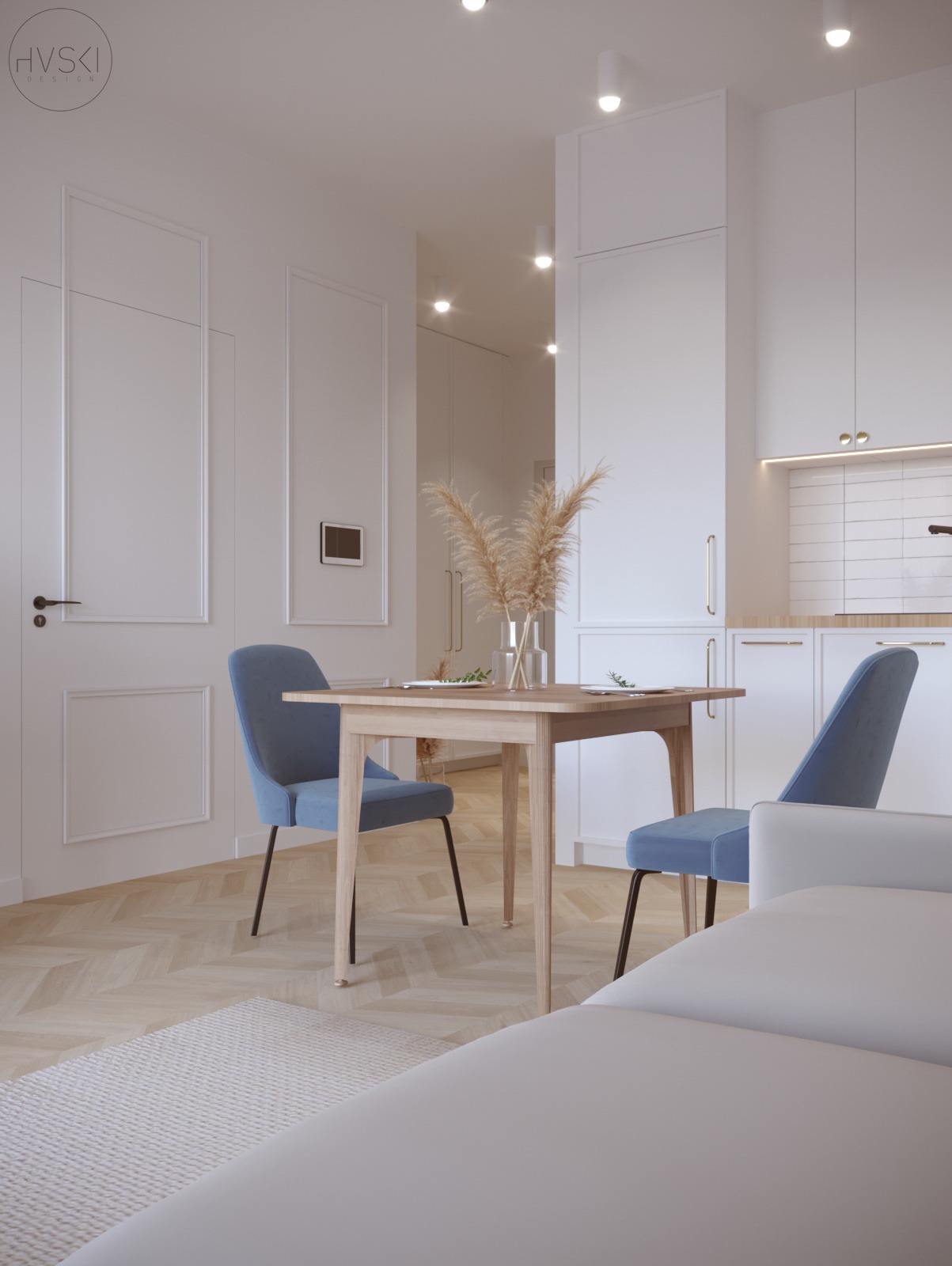 Jasne wnętrze mieszkania z drewnianą podłogą w jodełkę, błękitnymi krzesłami przy drewnianym stole z dekoracją z traw pampasowych w szklanym wazonie, widok na minimalistyczną kuchnię w tle.