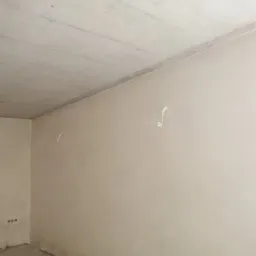 Gładka, jasna ściana wewnętrzna po mechanicznym nałożeniu tynku, widoczne ślady po usuniętych elementach instalacji elektrycznej.