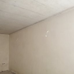 Gładka, jasna ściana wewnętrzna po mechanicznym nałożeniu tynku, widoczne ślady po usuniętych elementach instalacji elektrycznej.