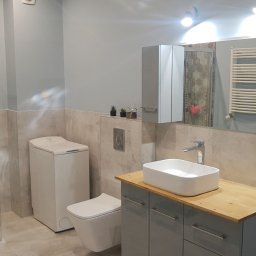 LaSerek Marcin Serafin - Nowoczesna łazienka w odcieniach szarości i beżu z kabiną prysznicową z heksagonalnymi płytkami, umywalką nablatową na drewnianym blacie i wiszącą toaletą.