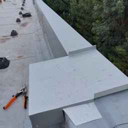 Sg-Bud - Montaż obróbek blacharskich na dachu hali, widoczne nożyce do blachy z pomarańczowymi uchwytami i krople deszczu na powierzchni blachy.