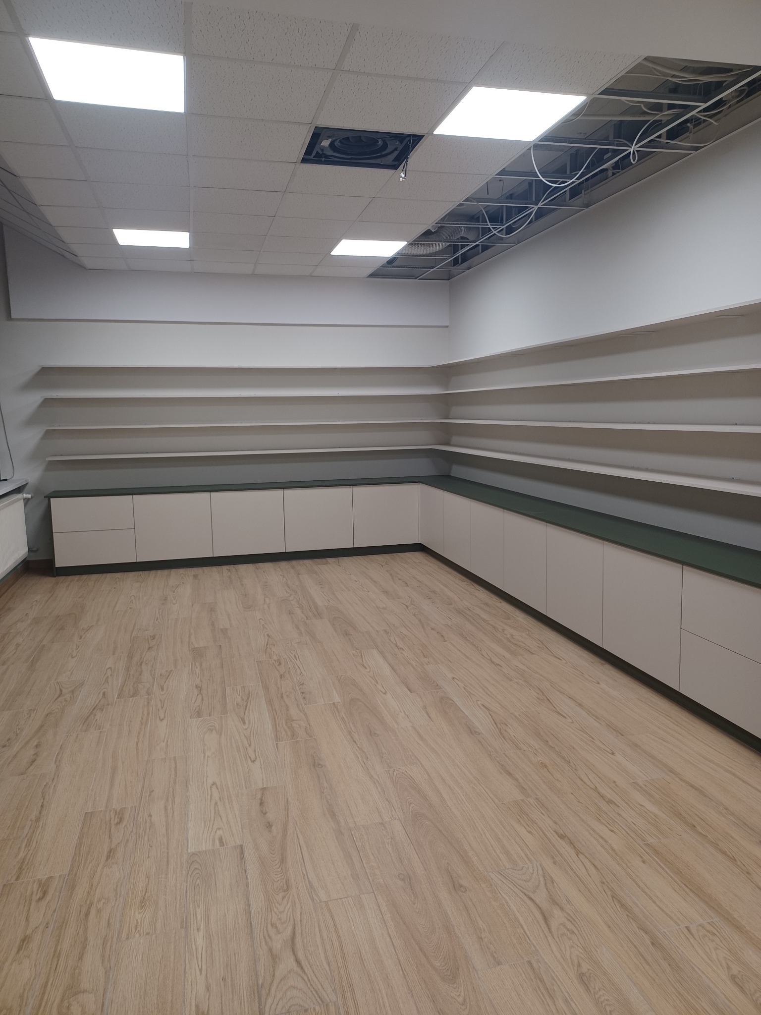 Wnętrze pomieszczenia z zamontowanymi szafkami i półkami wzdłuż ścian, widoczne niedokończone prace przy suficie podwieszanym.