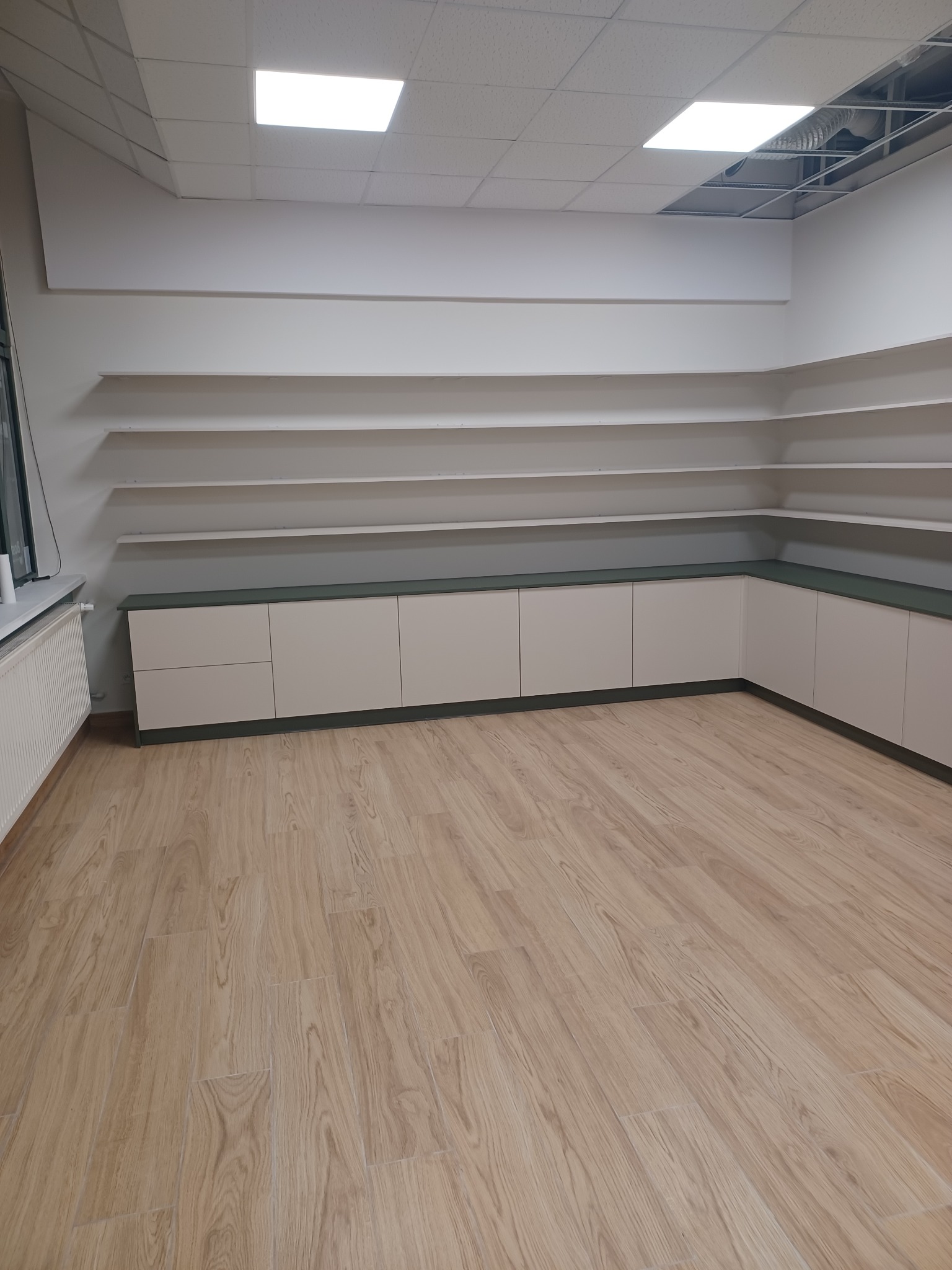 Beżowe szafki z ciemnozielonym blatem w nowym lokalu, widoczne półki pod sufitem i surowy strop z instalacjami.