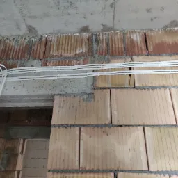 Wewnętrzna ściana z cegły dziurawki z ułożonymi przewodami elektrycznymi w białych peszlach, widoczne surowe wykończenie i otwór drzwiowy.