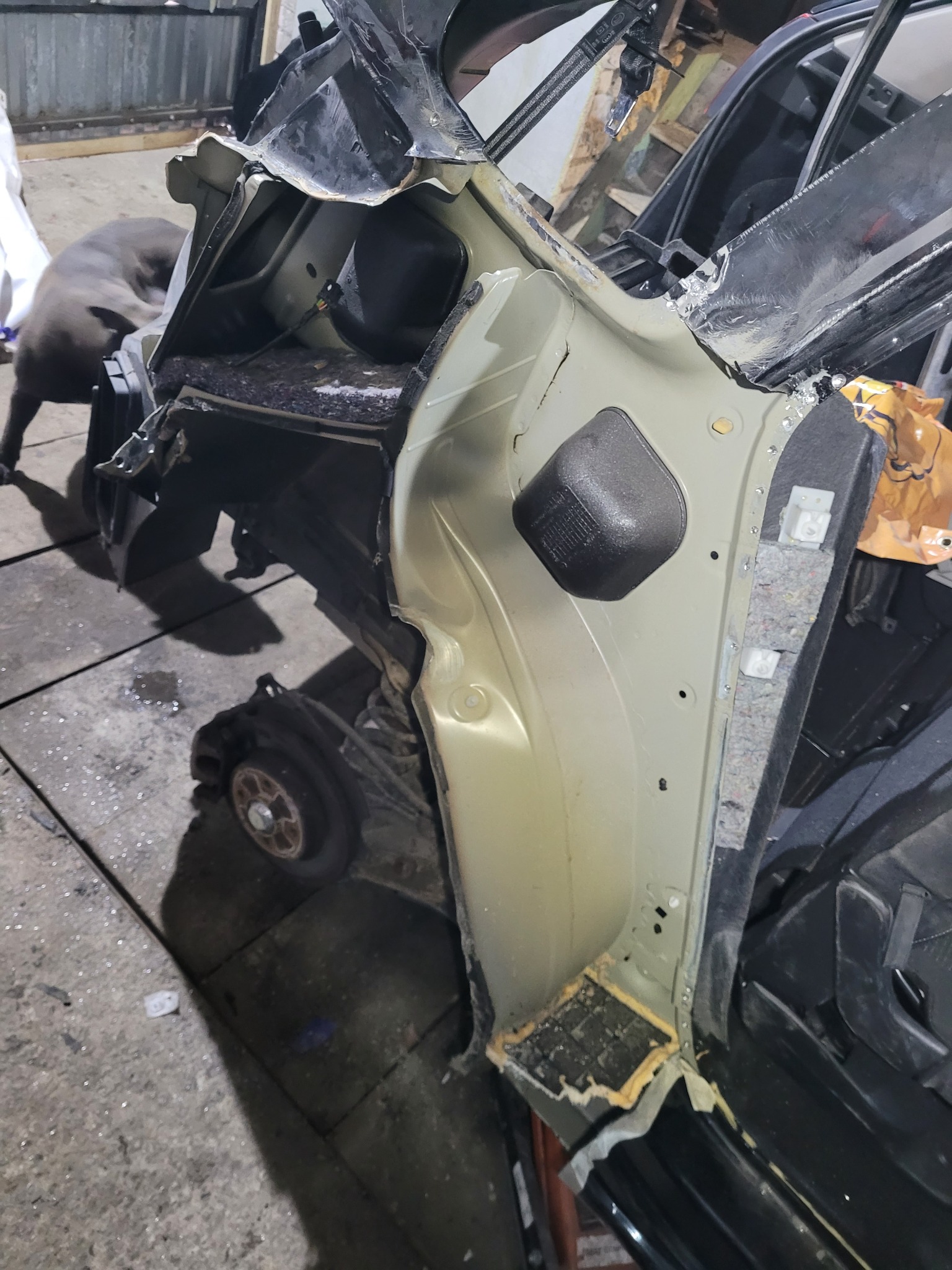 Uszkodzony samochód po wypadku, widoczne zniszczenia karoserii, brak koła, wnętrze pojazdu zdemontowane, w tle pies