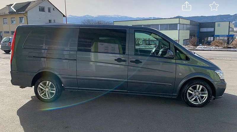 Szary van Mercedes Vito zaparkowany na zewnątrz, z widocznym budynkiem w tle i górami w oddali.