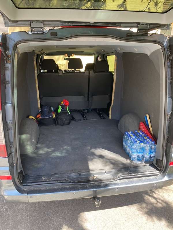 Wnętrze bagażnika samochodu dostawczego z widocznymi torbami, plecakami i zgrzewką wody mineralnej, gotowe do załadunku.