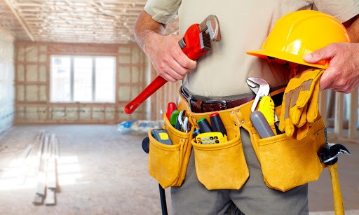 Mężczyzna z pasem narzędzi, kluczem nastawnym i kaskiem na tle surowego wnętrza w trakcie remontu.