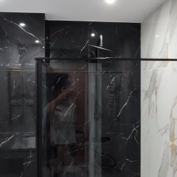 GlazuraProArt - Nowoczesna łazienka z kabiną prysznicową typu walk-in, wykończona płytkami imitującymi marmur w kolorze czarnym i białym, z czarną armaturą i oświetleniem punktowym.
