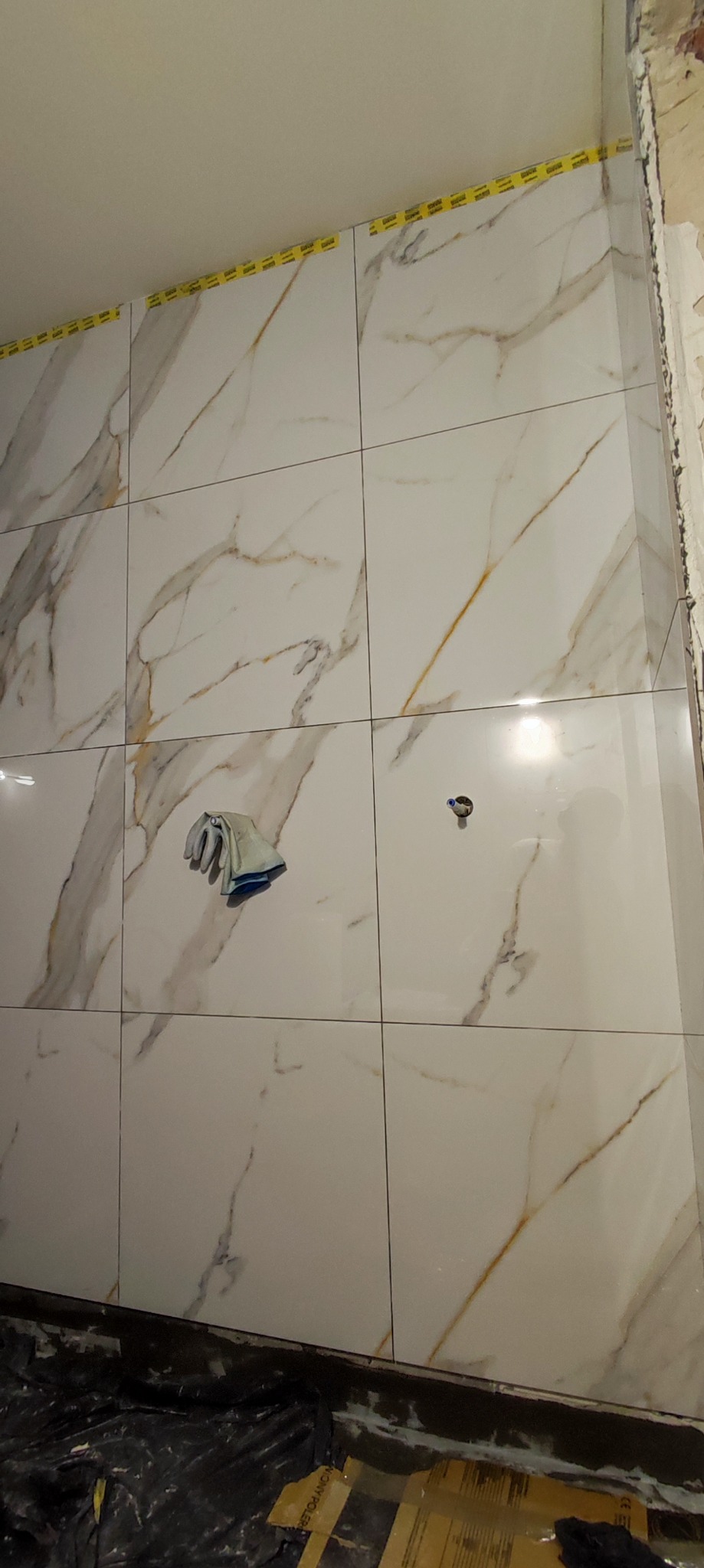 Ściana w trakcie układania płytek imitujących marmur w Legnicy, widoczna szmatka do czyszczenia i taśma maskująca przy suficie.