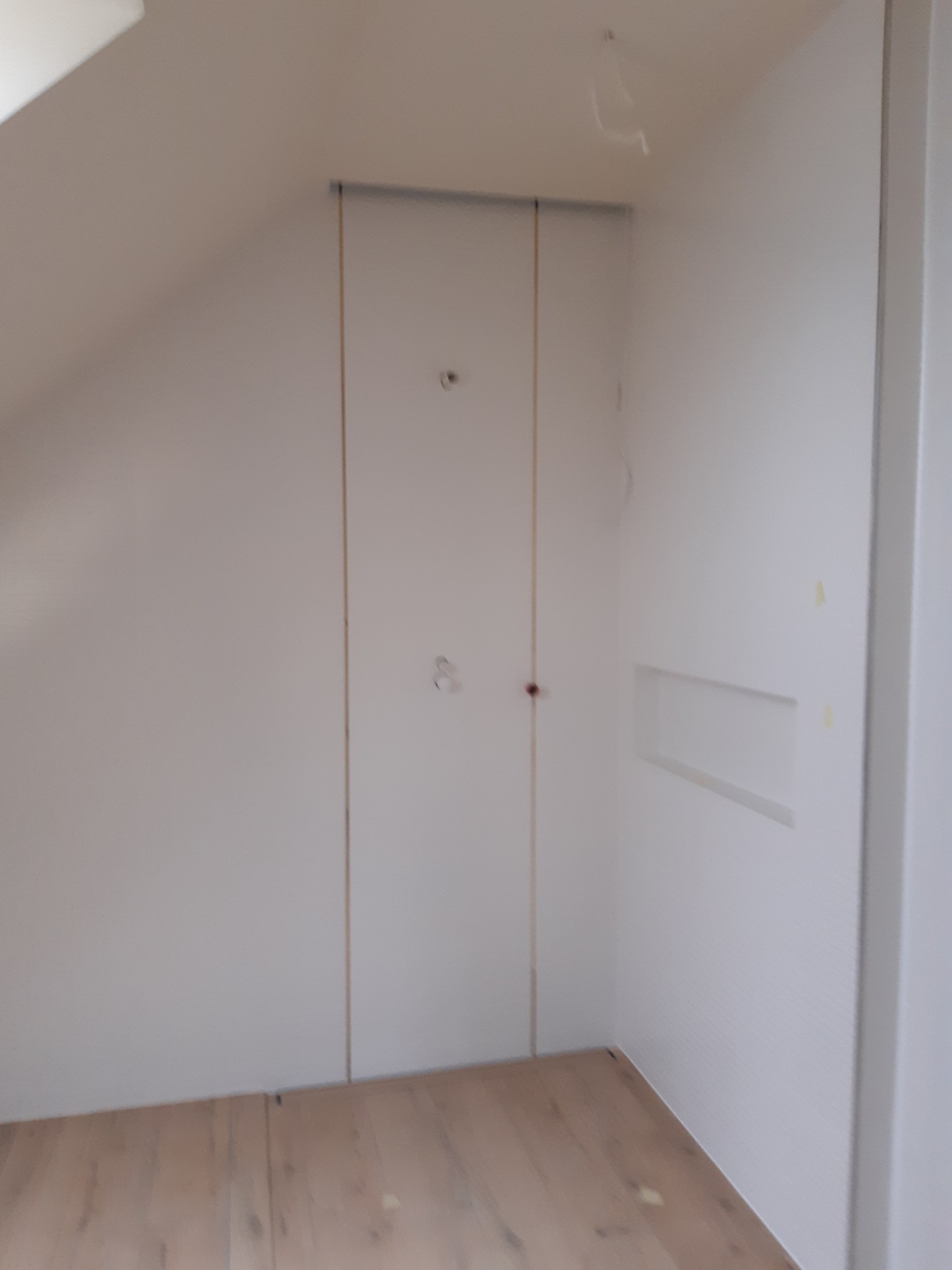 Wnętrze pokoju na poddaszu z drewnianą podłogą i białymi ścianami z zamontowaną płytą kartonowo-gipsową, widoczne ślady po szpachlowaniu i niedokończone wykończenia.