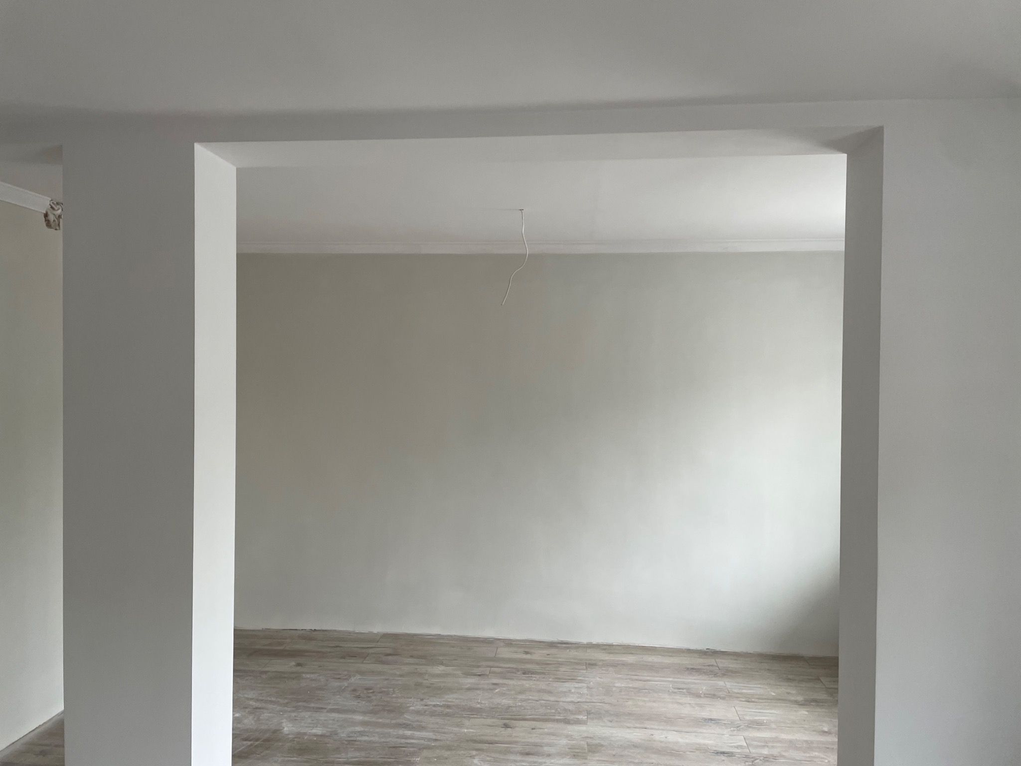Wnętrze po malowaniu na szaro, widoczne drewnopodobne panele podłogowe, białe ściany i sufit z listwą dekoracyjną, wystający kabel oświetleniowy.