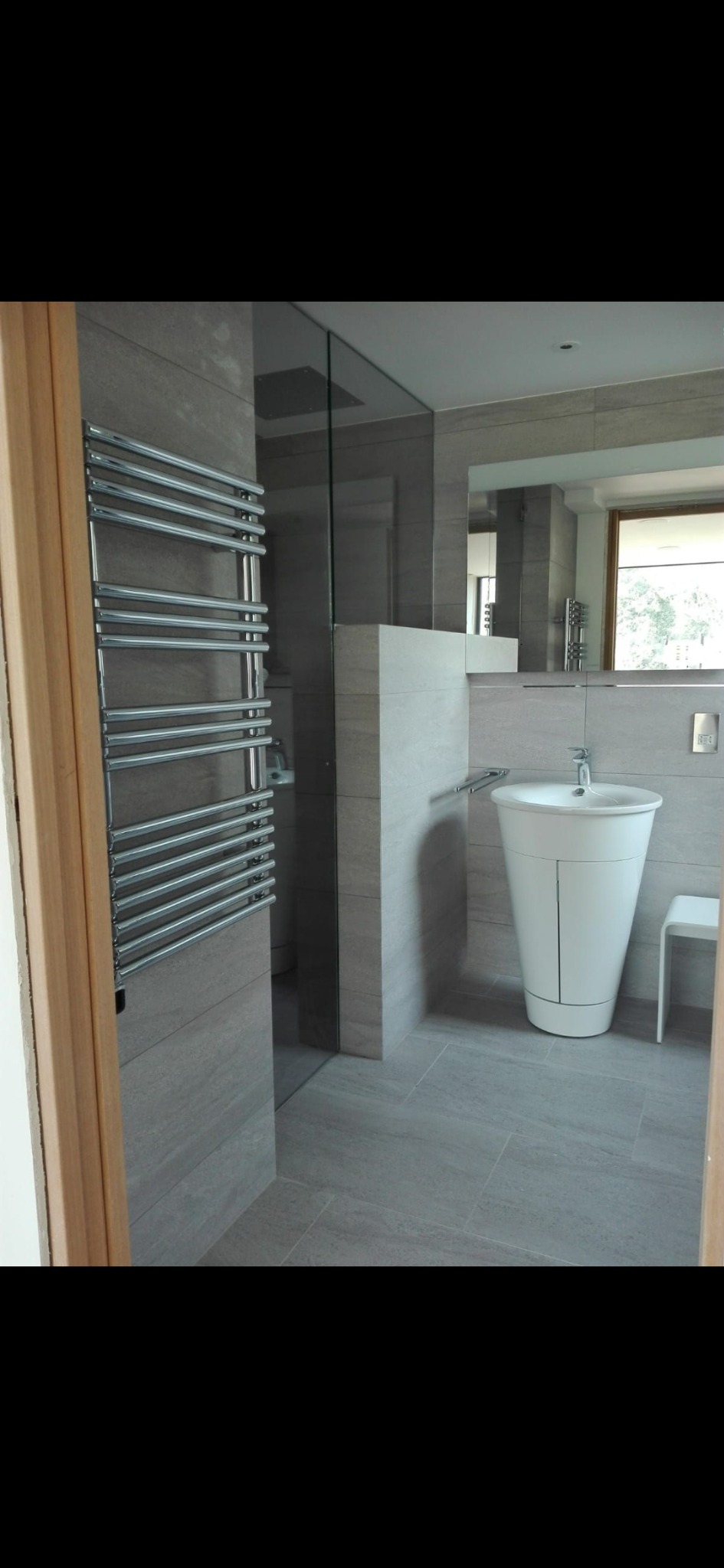 Nowoczesna łazienka w odcieniach szarości z podwieszaną umywalką na postumencie, grzejnikiem drabinkowym i kabiną prysznicową typu walk-in oddzieloną szklaną ścianką.