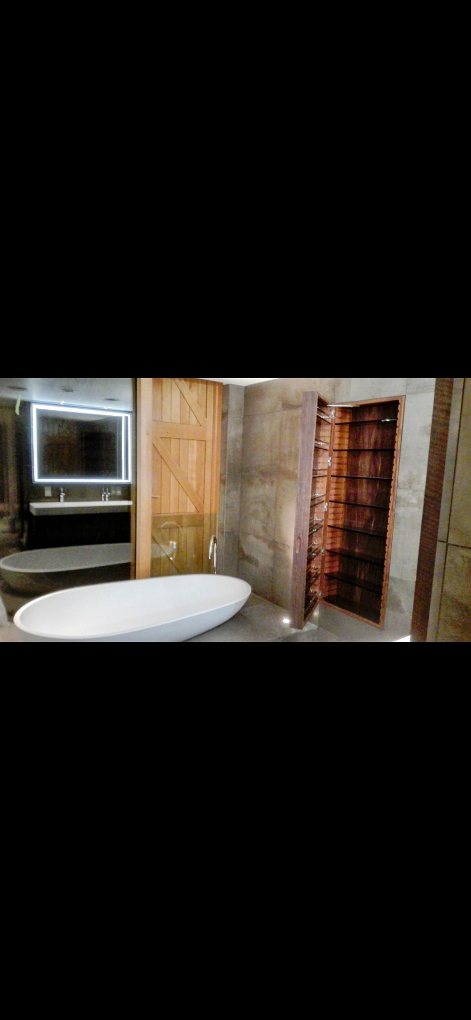 Nowoczesna łazienka z wolnostojącą białą wanną, drewnianą szafką z półkami i podświetlanym lustrem nad umywalką.