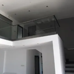 Wnętrze biura z antresolą: białe ściany, szklane balustrady, schody prowadzące na górę, minimalistyczne oświetlenie sufitowe.