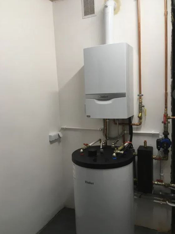 Kocioł gazowy kondensacyjny Vaillant zamontowany na białej ścianie, z widocznym zasobnikiem ciepłej wody i miedzianymi rurami.