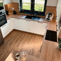 Honesto - Nowoczesna kuchnia w jasnych barwach z drewnianymi akcentami, widok z góry, z czarnym oknem i wyposażeniem kuchennym.