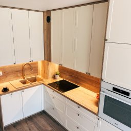 Honesto - Nowoczesna kuchnia w odcieniach bieli i drewna z złotą armaturą, czarną płytą indukcyjną i drewnianą podłogą, widziana z góry.