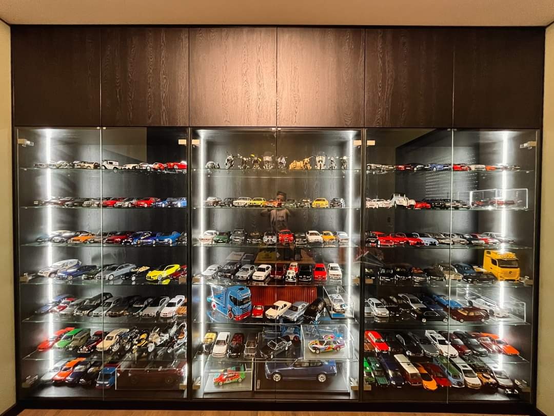 Półki z ciemnego drewna zabudowane od podłogi do sufitu, wypełnione kolekcją modeli samochodów, oświetlone punktowymi lampkami LED.