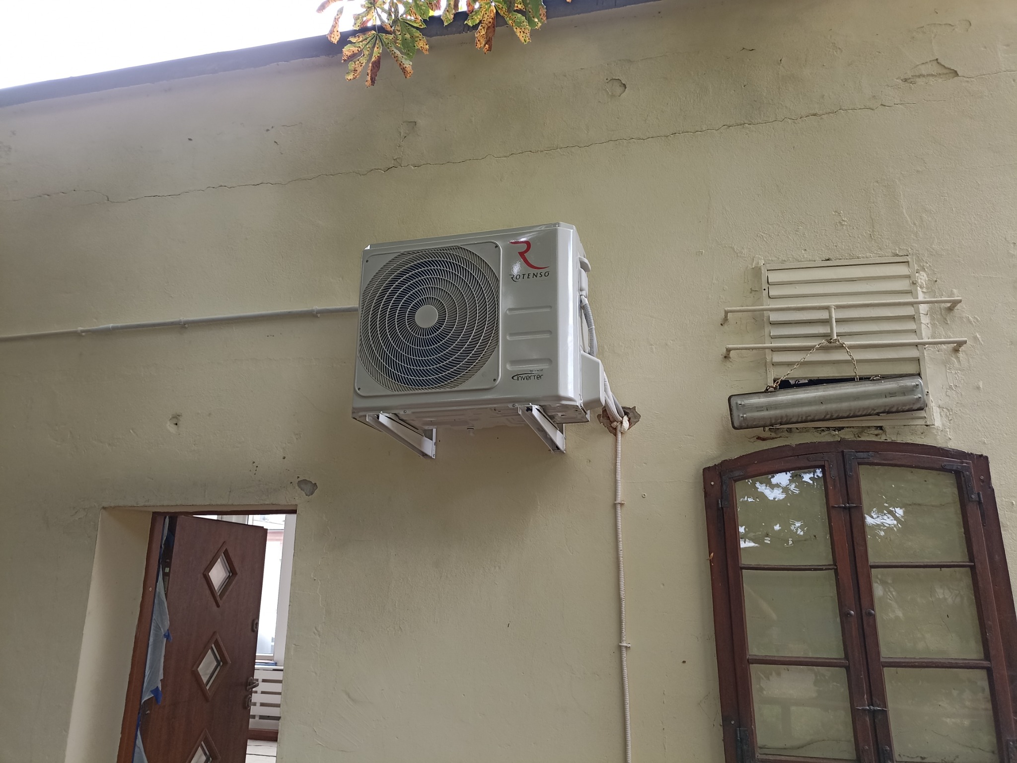 Zamontowany klimatyzator Rotenso na elewacji budynku we Wrocławiu, widoczne okno i otwarte drzwi w tle.