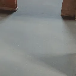 Wygładzona szara powierzchnia w surowym wnętrzu z ceglanymi ścianami, widoczna maszyna do polerowania posadzek z niebieskim silnikiem.