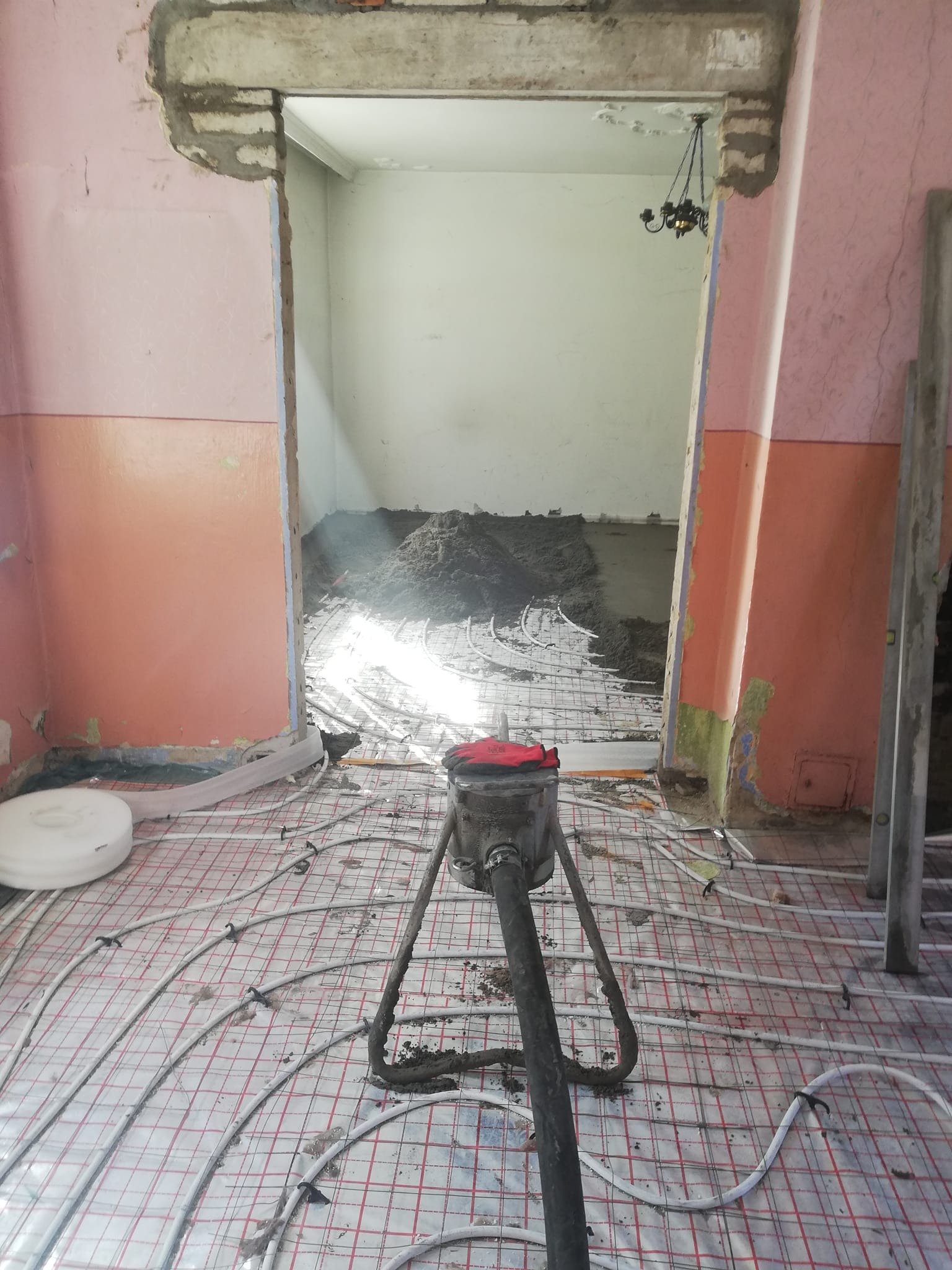 Aplikacja wylewki jastrychowej na ogrzewanie podłogowe w remontowanym pomieszczeniu z widocznymi elementami instalacji i urządzeniem do wylewania.