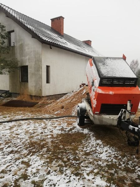 Pompa do wylewki stoi na zewnątrz budynku w zimowy dzień, w tle widoczny dom jednorodzinny z ceglanym kominem.