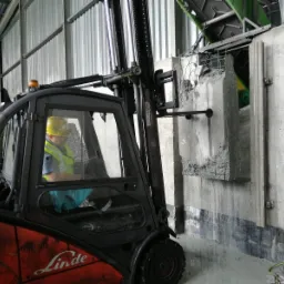 Operator w wózku widłowym Linde manewruje fragmentem wyciętej betonowej ściany z widocznym zbrojeniem, w tle konstrukcja hali.