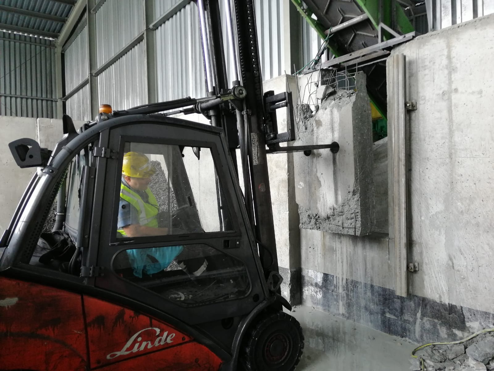 Operator w wózku widłowym Linde manewruje fragmentem wyciętej betonowej ściany z widocznym zbrojeniem, w tle konstrukcja hali.