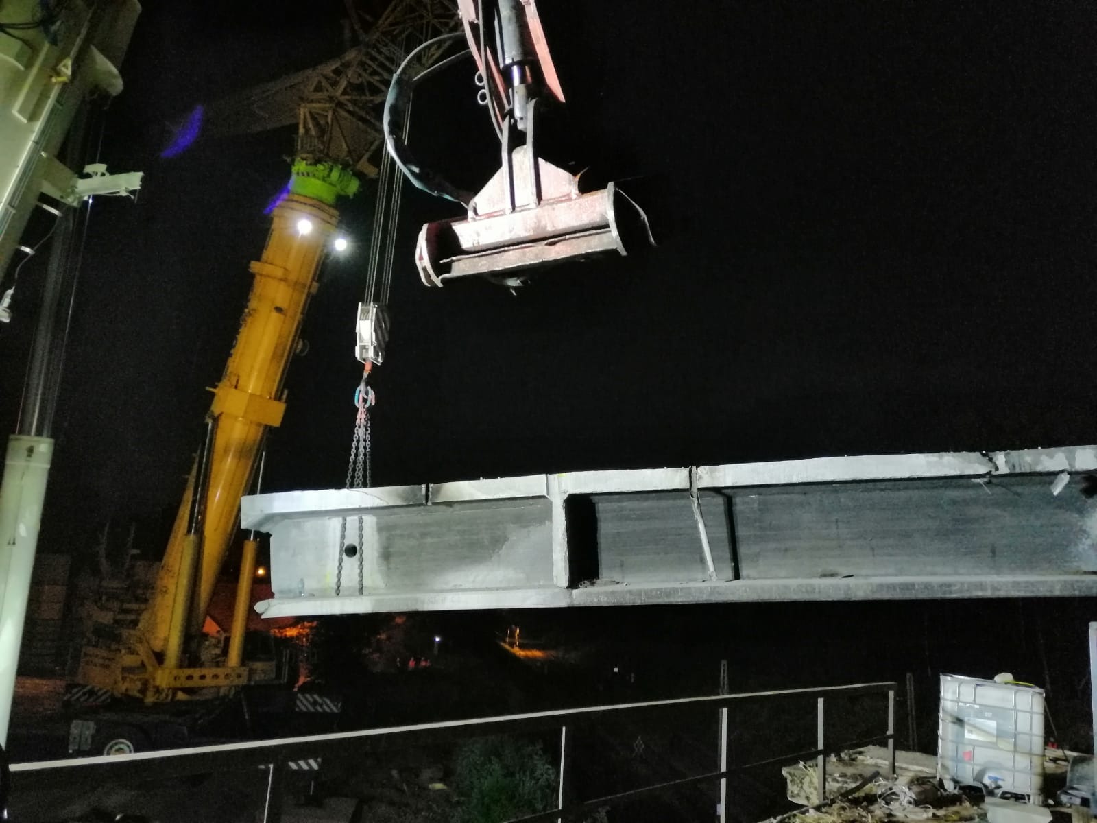 Żuraw w Katowicach podnosi betonowy element konstrukcyjny na tle nocnego nieba.