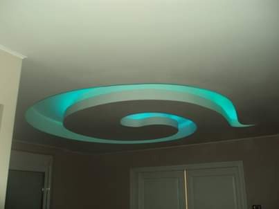 Spiralny sufit podwieszany z podświetleniem LED w kolorze turkusowym, widok z dołu, neutralne ściany i drzwi w tle.