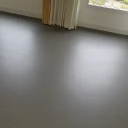 Gładka, szara podłoga w pustym pokoju z oknem i jasnymi zasłonami, widok z góry na świeżo umytą powierzchnię.