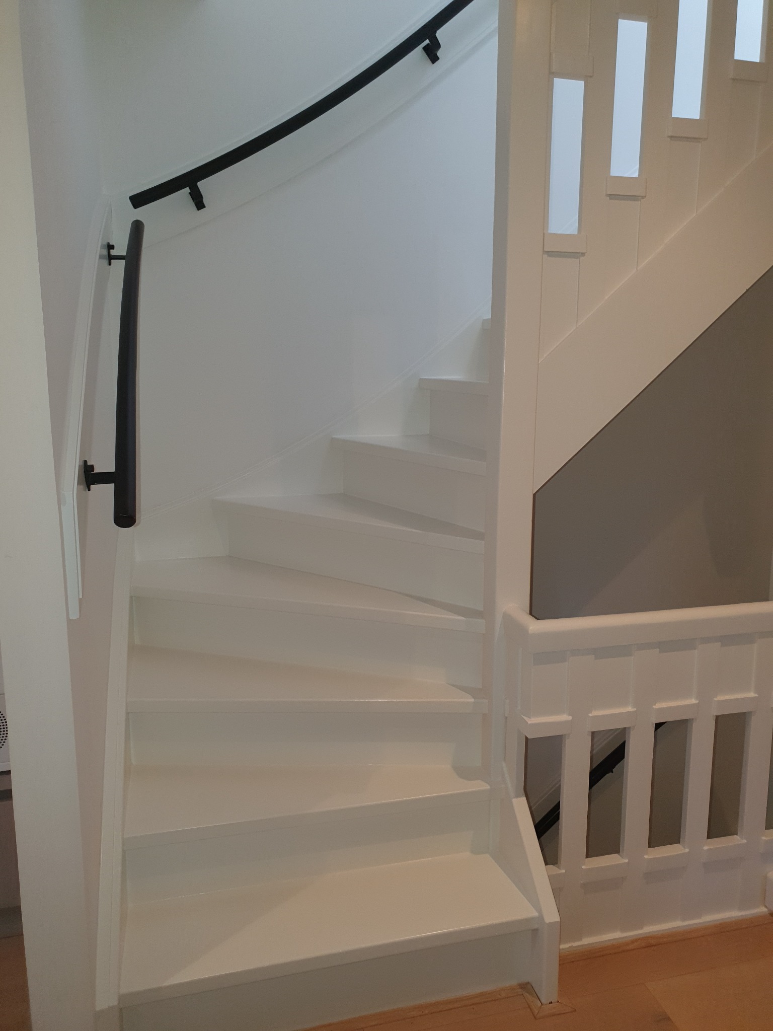 Białe, odnowione schody z czarną, zakrzywioną poręczą, widok z dołu.