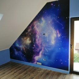 BIADACZ Paweł Biadacz - Pokój z fototapetą przedstawiającą kosmos na skośnej ścianie, podłoga z paneli, niebieskie wykończenie ścian, widoczne gniazdka elektryczne i przewody.