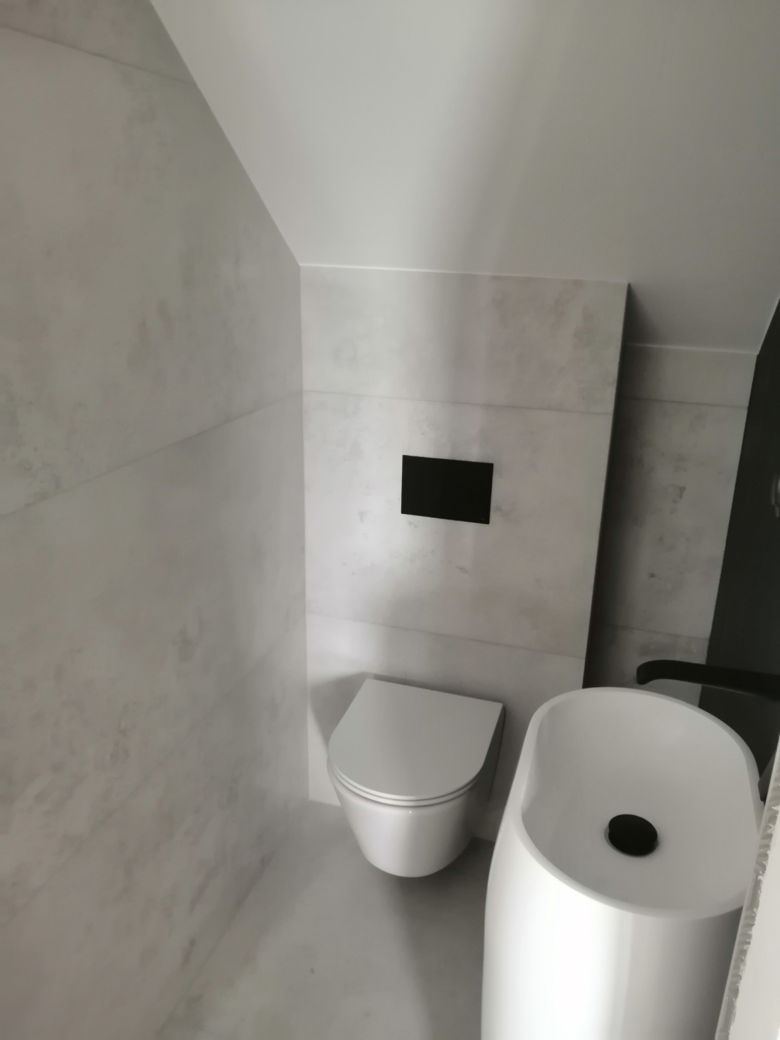 Nowoczesna łazienka na poddaszu z umywalką wolnostojącą, podwieszaną toaletą i szarymi płytkami imitującymi beton.