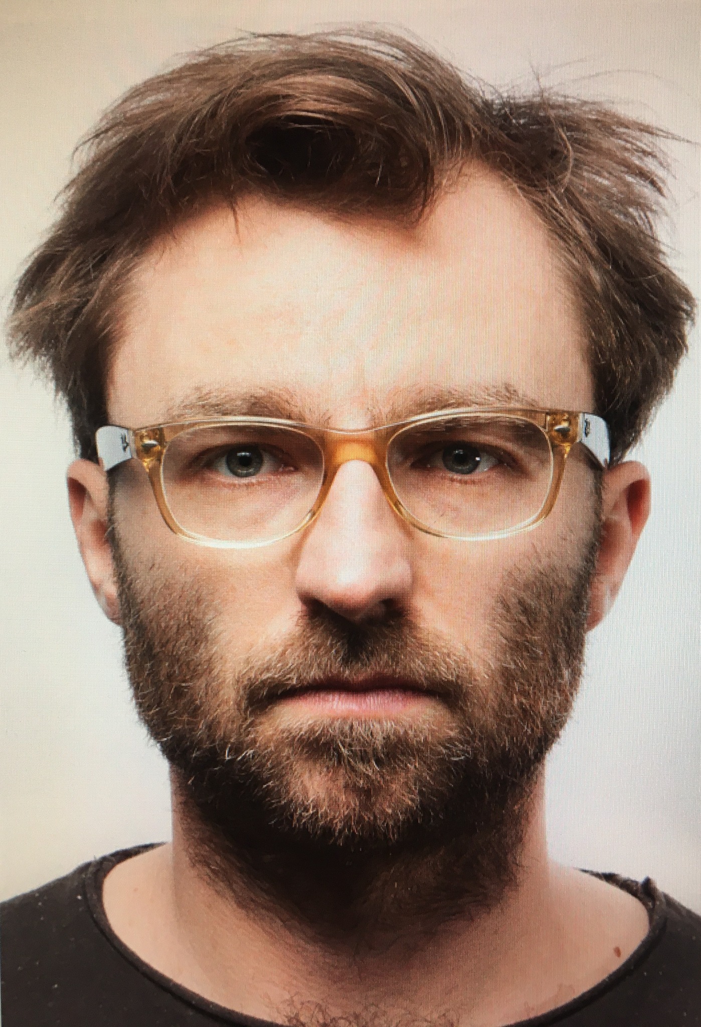 Portret mężczyzny z brodą i okularami w bursztynowych oprawkach na jasnym tle.