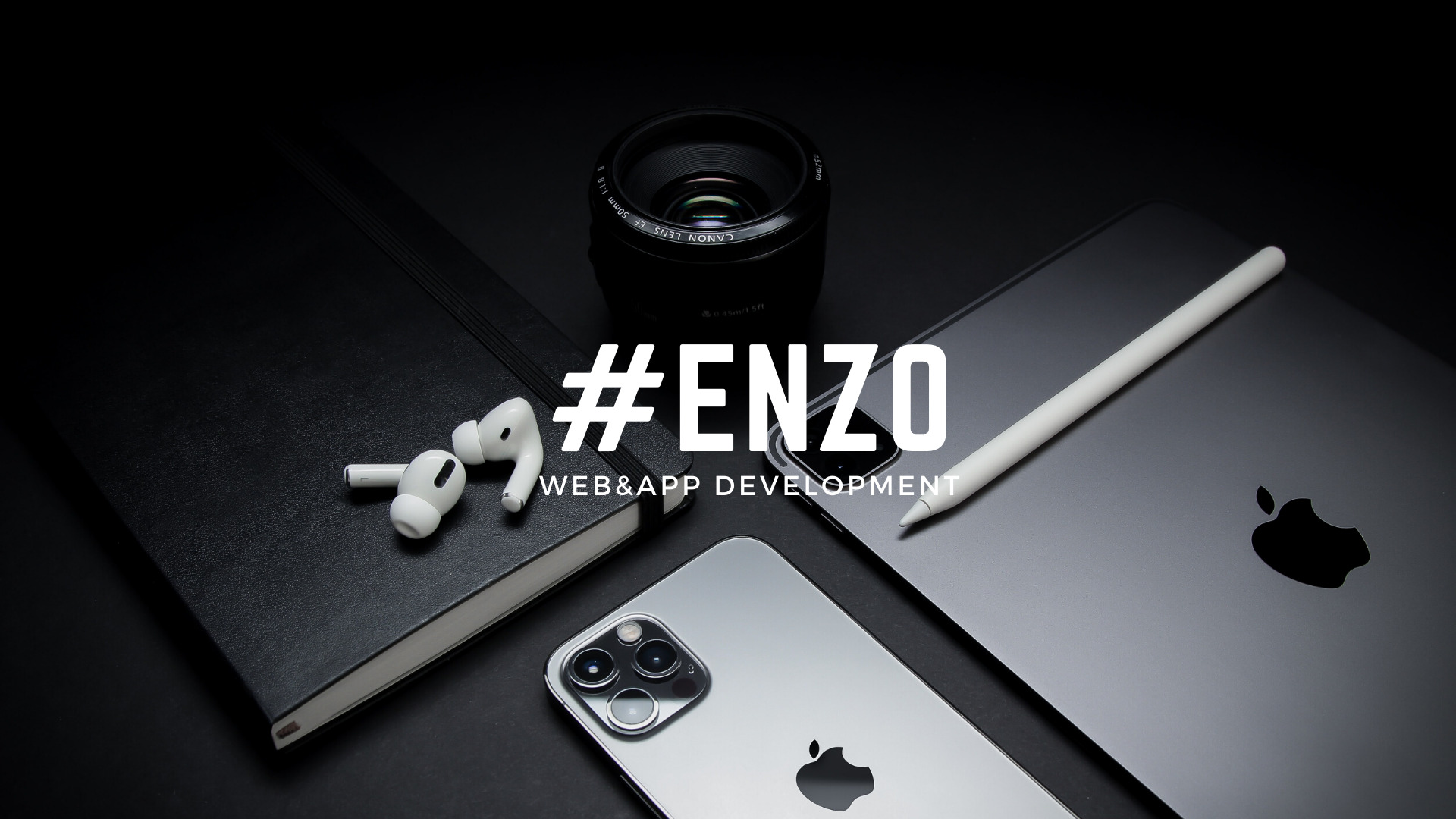 Aranżacja biurka z iPadem, iPhonem, słuchawkami AirPods, obiektywem aparatu i notatnikiem, na czarnym tle, z widocznym tekstem #ENZO WEB&APP DEVELOPMENT.