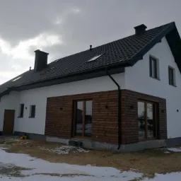 Nowoczesny dom jednorodzinny z białymi ścianami, drewnianą elewacją i dużymi oknami, widok z zewnątrz w zimowej scenerii.