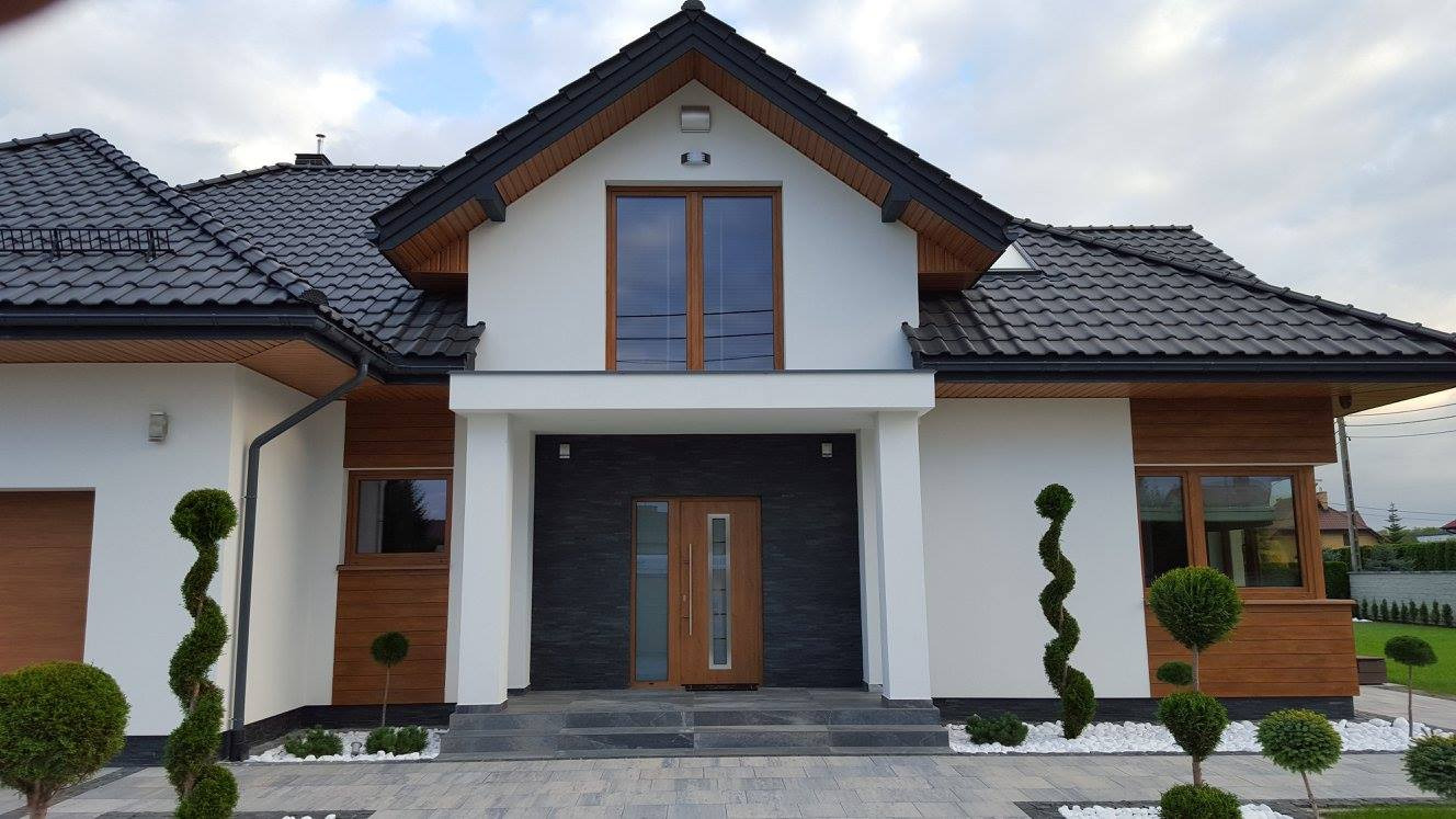 Elewacja domu jednorodzinnego z drewnianą stolarką okienną i bramą garażową z drewnianym wykończeniem, widok z poziomu chodnika, z dekoracyjnymi krzewami przed wejściem.