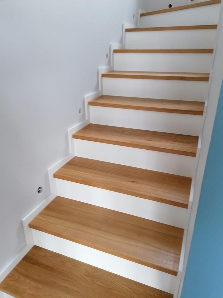 Schody drewniane z białymi podstopnicami, oświetlenie punktowe w ścianie, nowoczesny design.