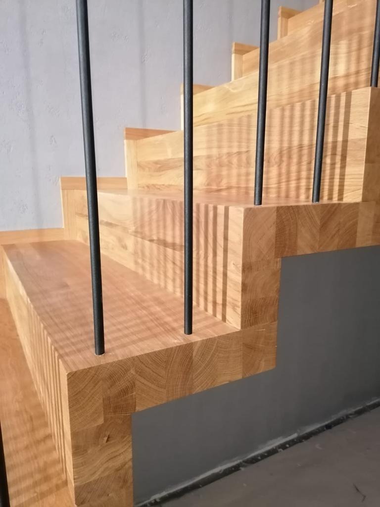 Nowoczesne schody dębowe z czarnymi, metalowymi balustradami, widok z dołu, z bliska, na tle szarej ściany.